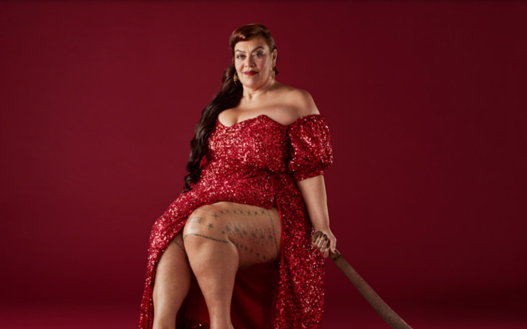 Publicity image for The Savage Coloniser Show, depicting a Samoan woman in a revealing glittery red dress, seated, holding a machete, against a blood-red background.