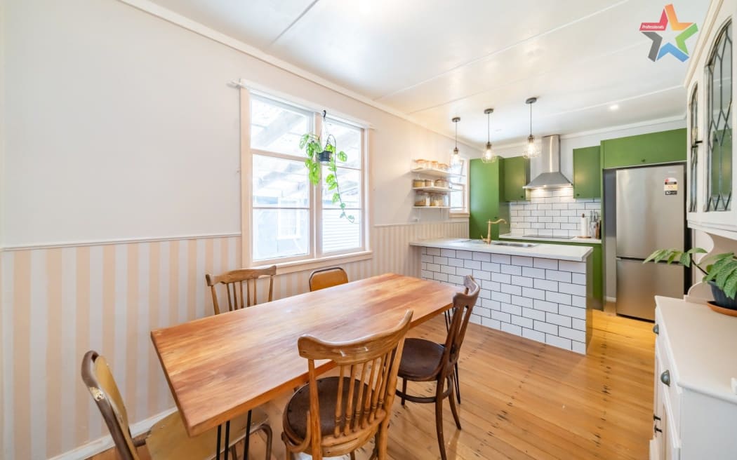 The interior of a home, the kitchen with a green wall and dining room with table and chairs.