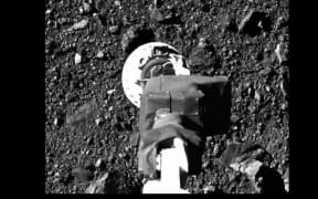 This NASA video frame grab handout image obtained on October 21, 2020 shows NASA's robotic arm from spacecraft Osiris-Rex making contact with asteroid Bennu to collect samples.