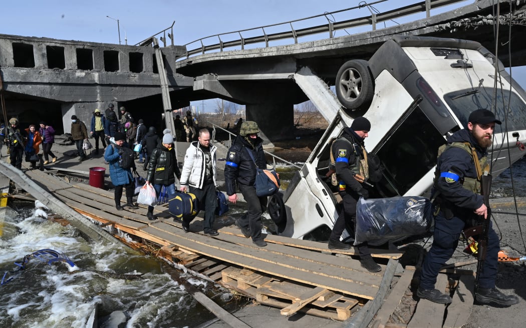 Ukrainian police officers help residents to cross a destroyed bridge as they evacuate Irpin, northwest of Kyiv, on 12 March 2022.