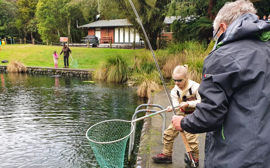 Isla Petersen learning to fish with Doug Stevens at the children's fishing pond near Turangi