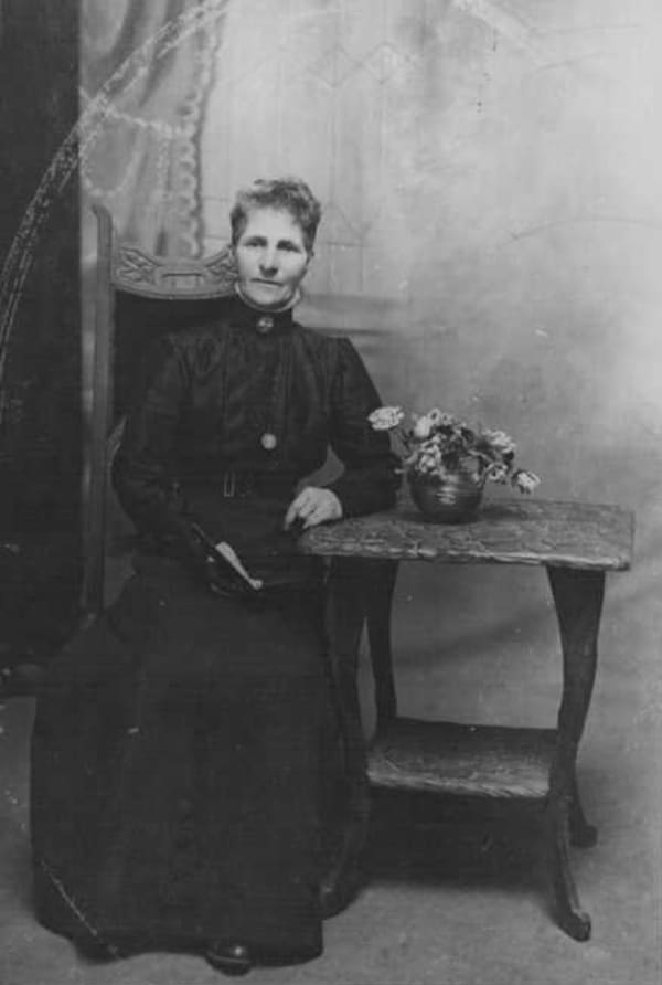 Fanny Osborne is a thin woman in a high-necked black gown resting against a side table.
