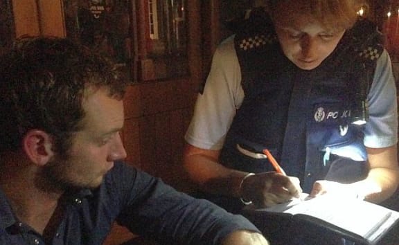 Female police officer kneels by young man seated on pavement to get more details