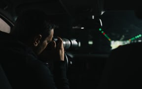 A generic photo of a man in his car doing surveillance with a camera.