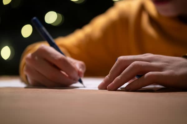 A person in an orange top writes with a pen on paper.