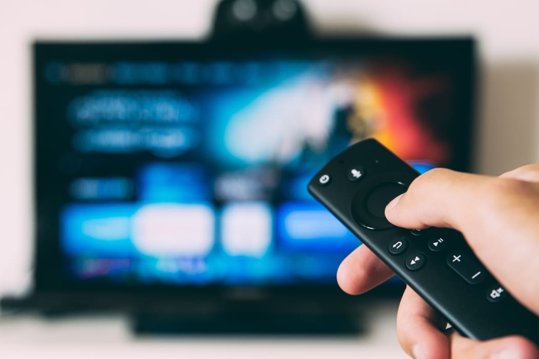 Someone pointing a remote at a television screen which is out of focus in the background.