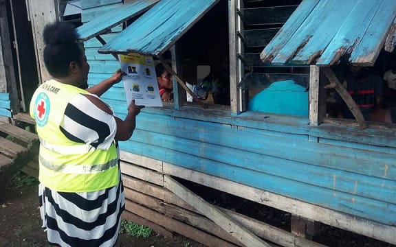 A Red Cross volunteer shares a message about Covid-19 transmissions through a window to a family in Uciwai Settlement, Nadi.