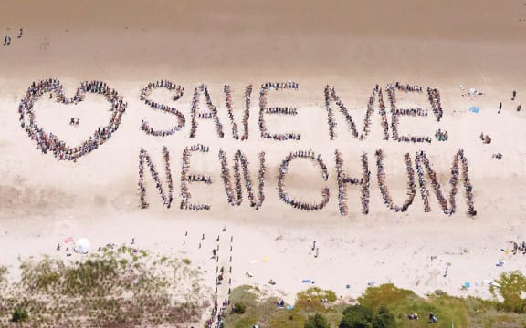 A group of people form the words "Save New Chum" on the beach. The photo is taken from the air.