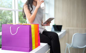 Woman is drinking a coffee and wilding the tablet phone with shopping bag at side for online shopping concept