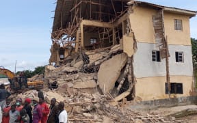 Bystanders gather next to the ruins of a school collapsed earlier in Jos, on July 12, 2024 as heavy machinery is seen at work on the site. At least 16 students were killed on Friday when a school in central Nigeria collapsed on pupils taking exams, according to an AFP correspondent. Trapped students were heard crying for help under the rubble after the Saint Academy school in Jos North district of Plateau State fell in on classrooms. (Photo by Muhammad Tanko Shittu / AFP)