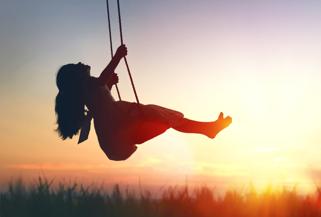 Happy laughing child girl on swing in sunset summer.