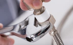A close-up of a plumber screwing a plumbing fitting onto a pipe