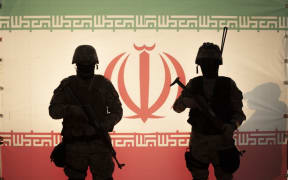 Two Islamic Revolutionary Guard Corps (IRGC) 
armed military personnel pose for a photograph in front of an Iran flag during a pro-government protest rally in southern Tehran, December 29, 2022. Pro-government protest rally held in support of Iran's Supreme Leader Ayatollah Ali Khamenei and in opposition to recent unrest following the death of Mahsa Amini, a 21-year-old Iranian-Kurd. (Photo by Morteza Nikoubazl/NurPhoto) (Photo by Morteza Nikoubazl / NurPhoto / NurPhoto via AFP)