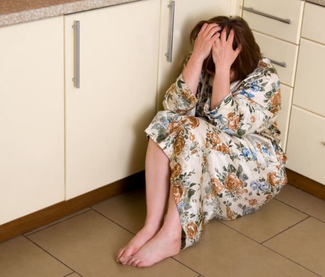 A woman sits on the kitchen floor with her head in her hands