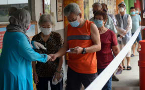 A presiding officer (left) checks voters' identity cards as they enter a school hall, temporarily used as a polling station, to cast their ballots during the general election in Singapore on July 10, 2020.