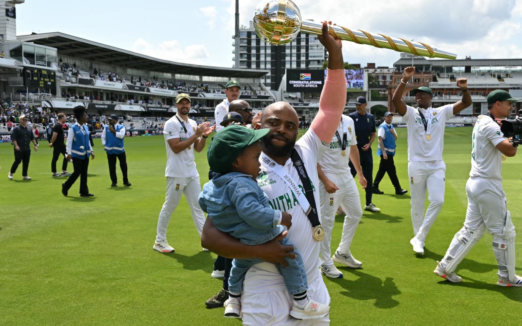 South Africa's captain Temba Bavuma holds his son and the ICC World Test Championship Mace as he celebrates with teammates after victory on day four of the ICC World Test Championship cricket final match between Australia and South Africa, at Lord's cricket ground, in London, on June 14, 2025. South Africa won the Test by 5 wickets. (Photo by Glyn KIRK / AFP) / RESTRICTED TO EDITORIAL USE. NO ASSOCIATION WITH DIRECT COMPETITOR OF SPONSOR, PARTNER, OR SUPPLIER OF THE ECB
