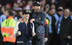 US actors and Wrexham owners Rob McElhenney (L) and Ryan Reynolds celebrate on the pitch after the English National League football match between Wrexham and Boreham Wood at the Racecourse Ground Stadium.