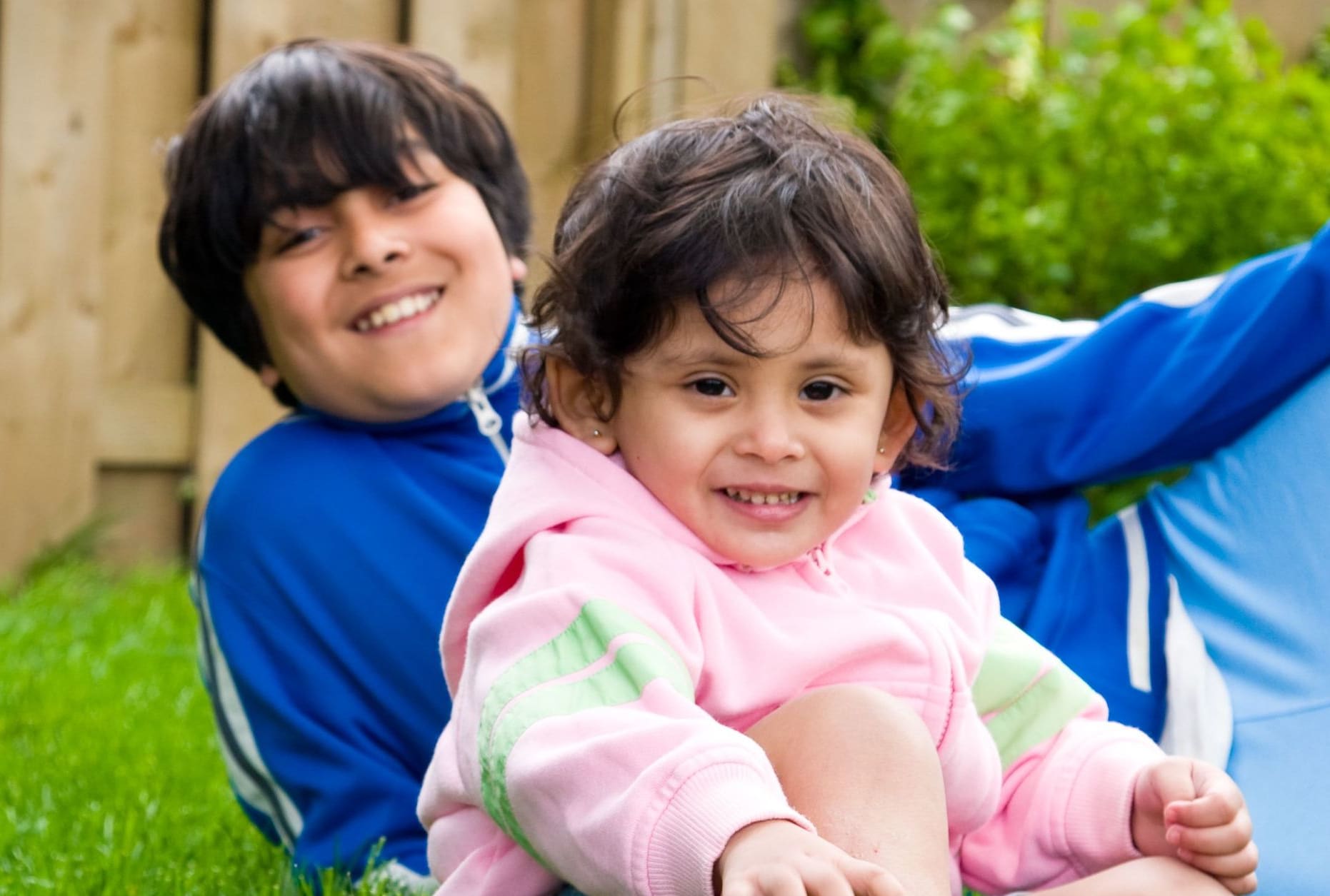 A photo of a young boy sitting in the backyard with his sister