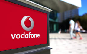 Street signage board with Vodafone logo. Blurred office center and walking people background. Editorial 3D rendering United States