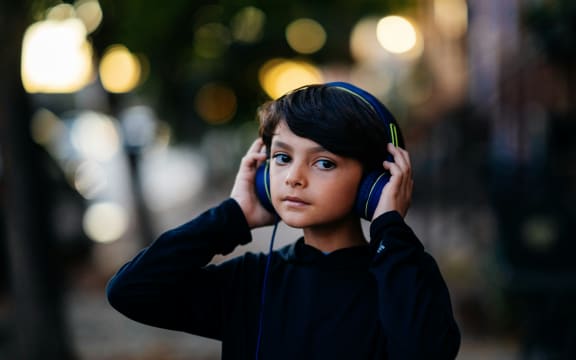A child listening to headphones, with their hands on each headphone, wearing a dark-coloured top.