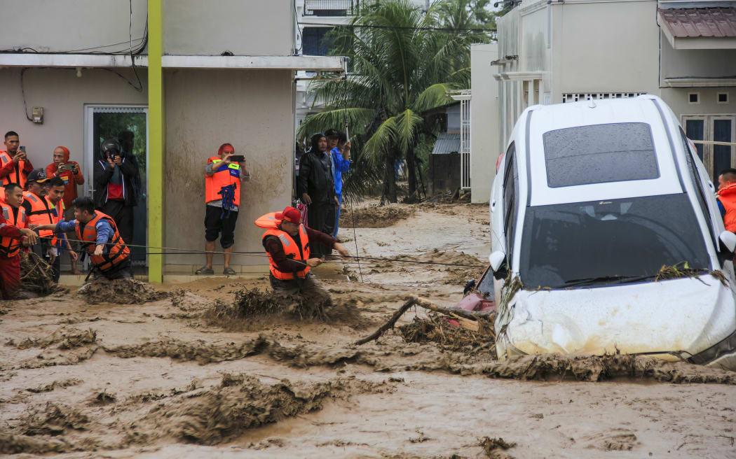 Rescuers wade through flood waters by holding a rope in their effort to evacuate residents who are trapped at their houses in Padang, West Sumatra province on November 27, 2025. (Photo by REZAN SOLEH / AFP)