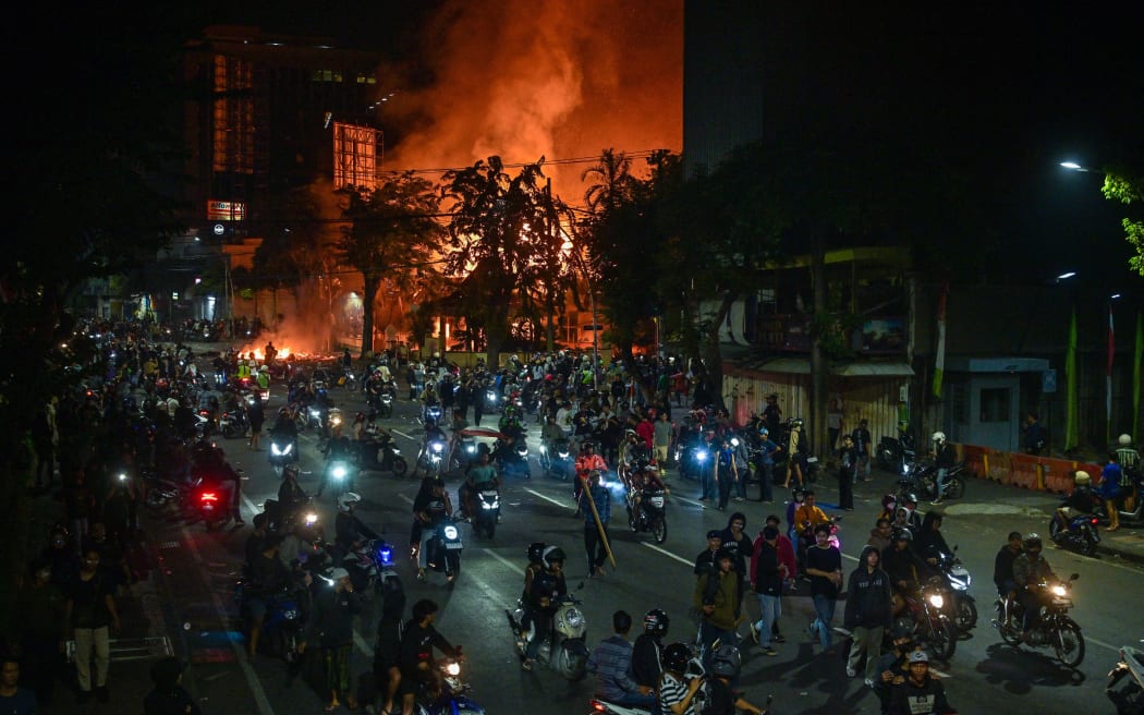 Protesters rides motorcycles in front of a police headquarters that was burned and looted during demonstrations in Surabaya.