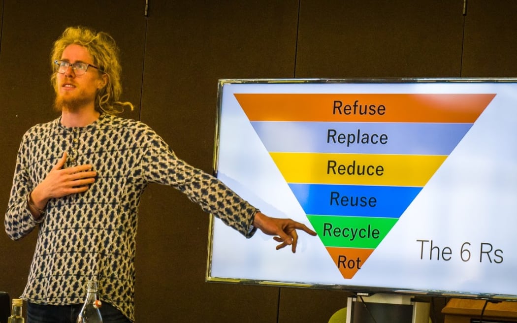 Liam Prince, founder of The Rubbish Trip, points to a presentation on compositing. The image on display is an inverted triangle with the labels, refuse, replace, reduce, reuse recycle and rot placed on it in descending order.