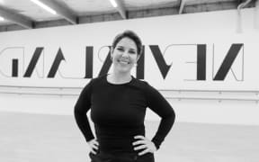 Ash is standing in her dance studio. She is wearing a black top with her hands on her hips. The photo has probably been revered becasue the wall behind her says neverland backwards, but maybe it was just painted like that. I haven't seen it in real life.