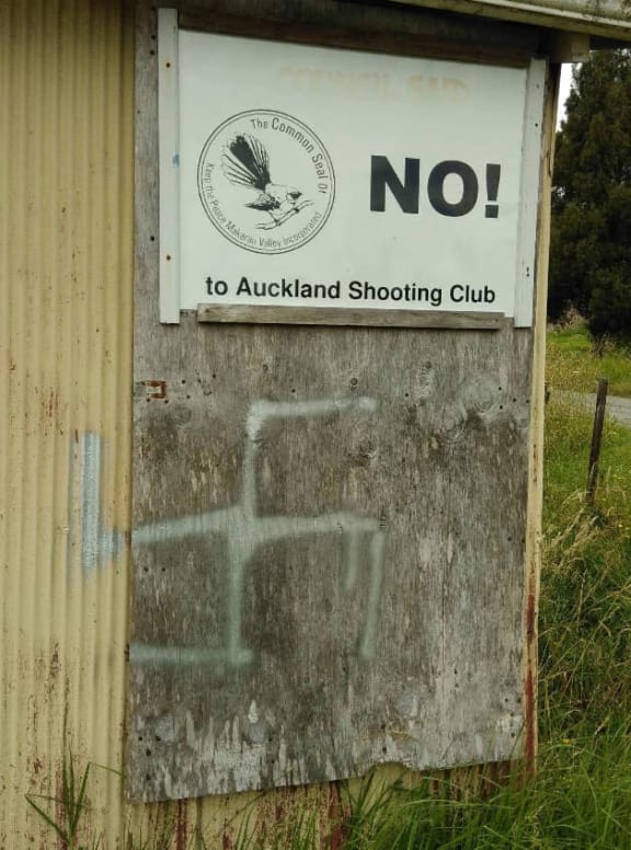 A swastika sprayed on to a shed with protest signs on the neighbouring property to the gun club.