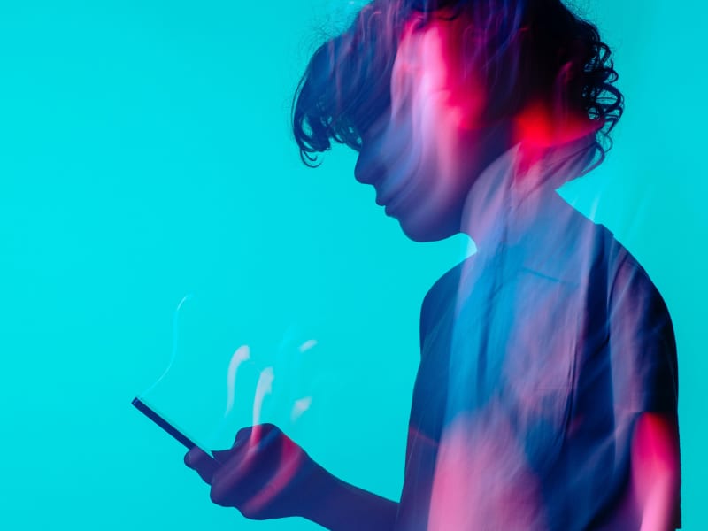 A silhouette of a teenager holding a cell phone.