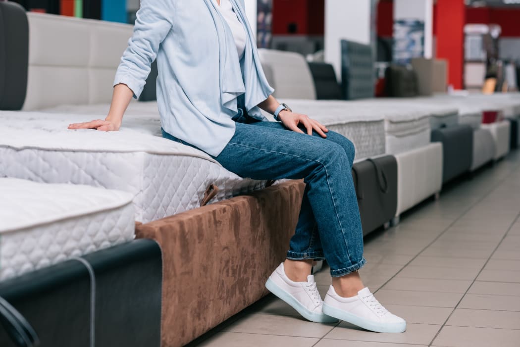 Shopper sits on mattress at furniture shop.