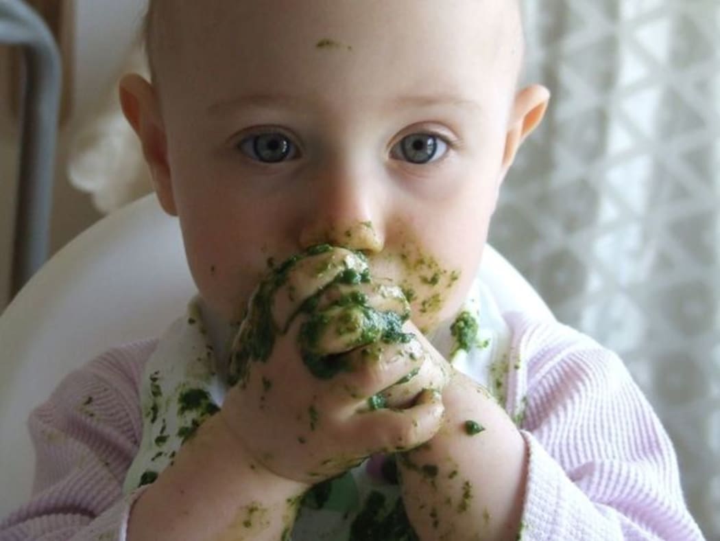 A photo of a toddler eating messy green food with her fingers
