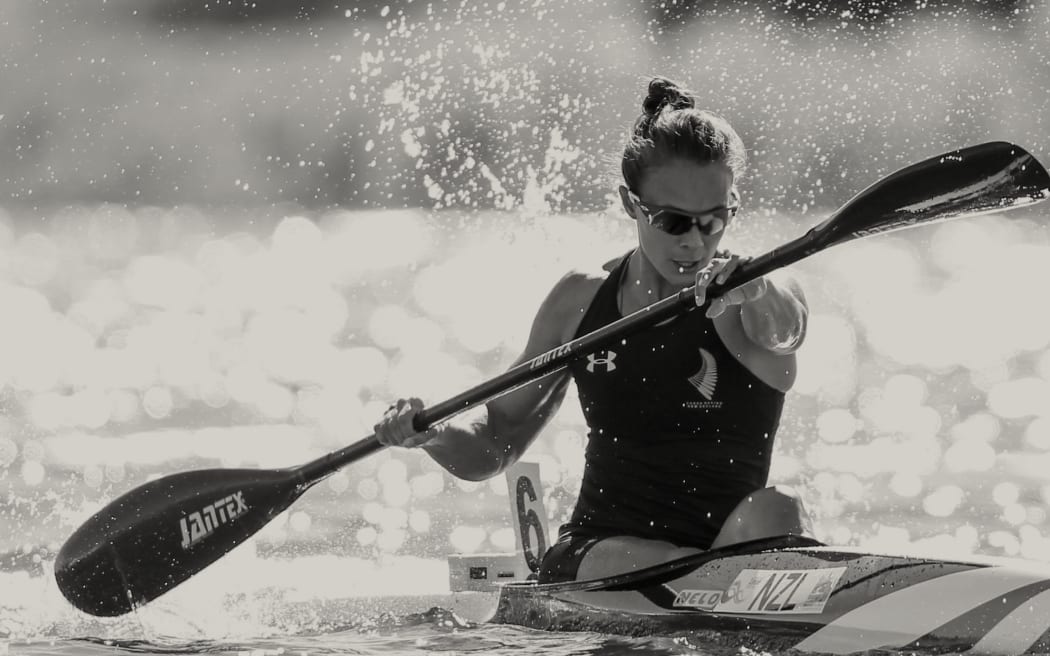 Close crop of Lisa Carrington rowing in a competitive race, water dappled in the background