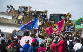 (FILES) Members of the Standing Rock Sioux Tribe and their supporters opposed to the Dakota Access Pipeline (DAPL) confront bulldozers working on the new oil pipeline in an effort to make them stop on September 3, 2016, near Cannon Ball, North Dakota. Nearly a decade after activists led one of the largest anti-pipeline protests in US history, the fight shifts to court as Energy Transfer sues Greenpeace for $300 million in a case with far-reaching free speech implications. At the center of the lawsuit is the Dakota Access Pipeline, which transports fracked crude oil from North Dakota to refineries and the global market. Controversial from its inception, the pipeline faced fierce opposition led by the Standing Rock Sioux tribe. Beginning in the spring of 2016, protests and legal challenges sought to block what the tribe called the “Black Snake,” warning it would threaten their ancestral lands. (Photo by Robyn BECK / AFP)