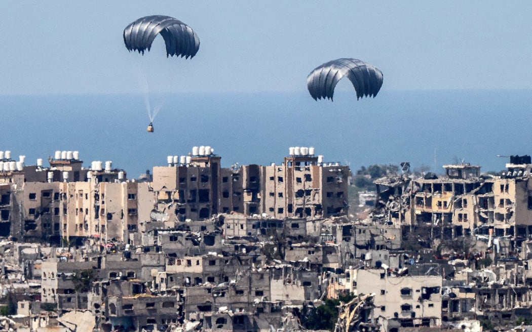 This picture taken from Israel's southern border with the Gaza Strip shows parachutes of humanitarian aid dropping over the besieged Palestinian territory on March 26, 2024, amid the ongoing conflict between Israel and the militant group Hamas. Seven people have drowned in the Mediterranean trying to reach aid airdropped into Gaza, the Hamas-run territory's health ministry said on March 26. Six people were also injured in the previous day's airdrop, the ministry said. Hamas said a total of 18 people have now been killed in drownings or stampedes since aid airdrops to the starving north of the besieged territory began. (Photo by JACK GUEZ / AFP)