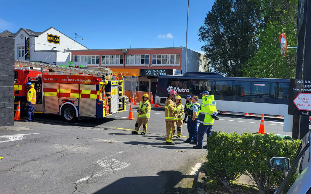 A number of firefighters and police officers can be seen standing by a road with fire engines and cones.