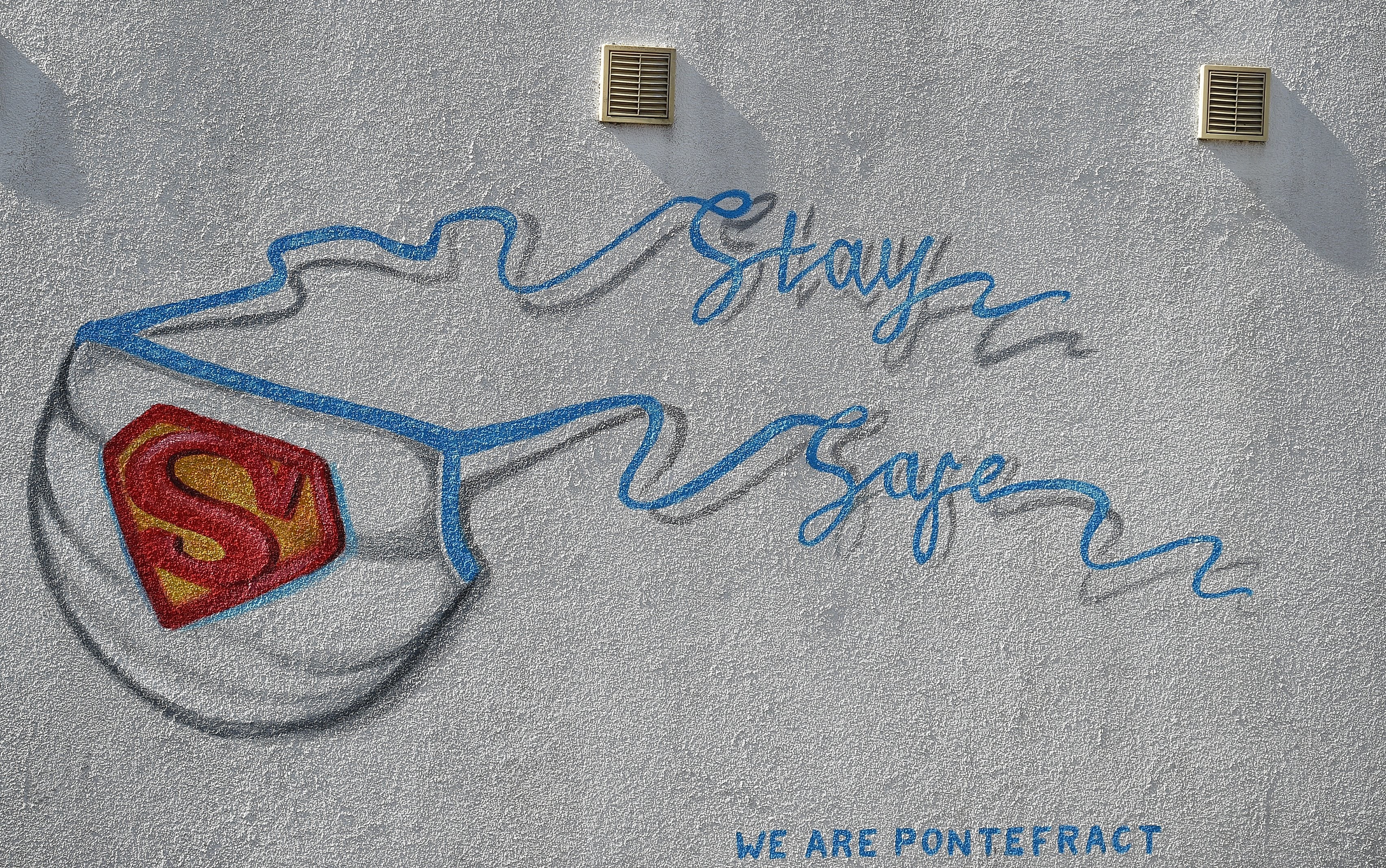 Graffiti depicting the badge of Superman and Superwoman, and forming a mask with the words "Stay Safe", on a wall in northern England on April 14, 2020.