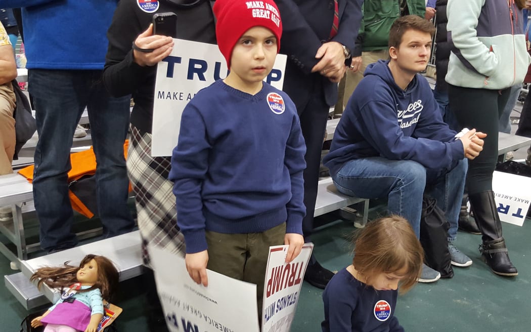 Young boy and his younger sister at a Trump rally wearing supporters buttons etc and holding flags