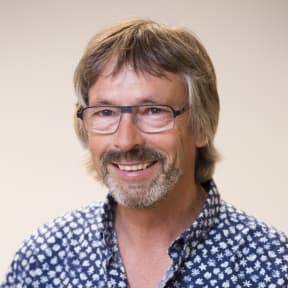 A headshot of a smiling man with sandy brown hair, facial hair and glasses.
