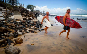 Two surfers negotiate massive beach erosion in the wake of cyclonic conditions at Byron Bay Main Beach on December 15, 2020, after wild weather lashed Australia's Northern New South Wales.