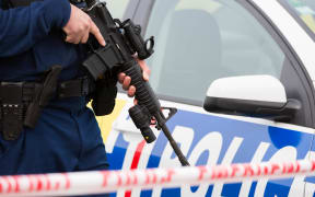 A police officer stands watch at the edge of a cordon of a crime scene holding a gun
