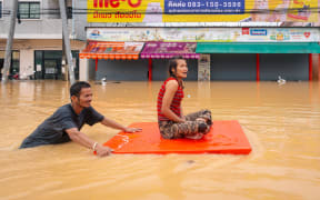 A man transports a woman through flood waters in Hat Yai in Thailand's southern Songkhla province on November 26, 2025, as severe flooding affected thousands of people in the country's south following days of heavy rain. Tens of thousands of people in Thailand and neighbouring Malaysia were displaced by widespread flooding, with streets submerged, homes inundated and at least 34 dead, officials said November 26. (Photo by Arnun Chonmahatrakool / THAI NEWS PIX / AFP)