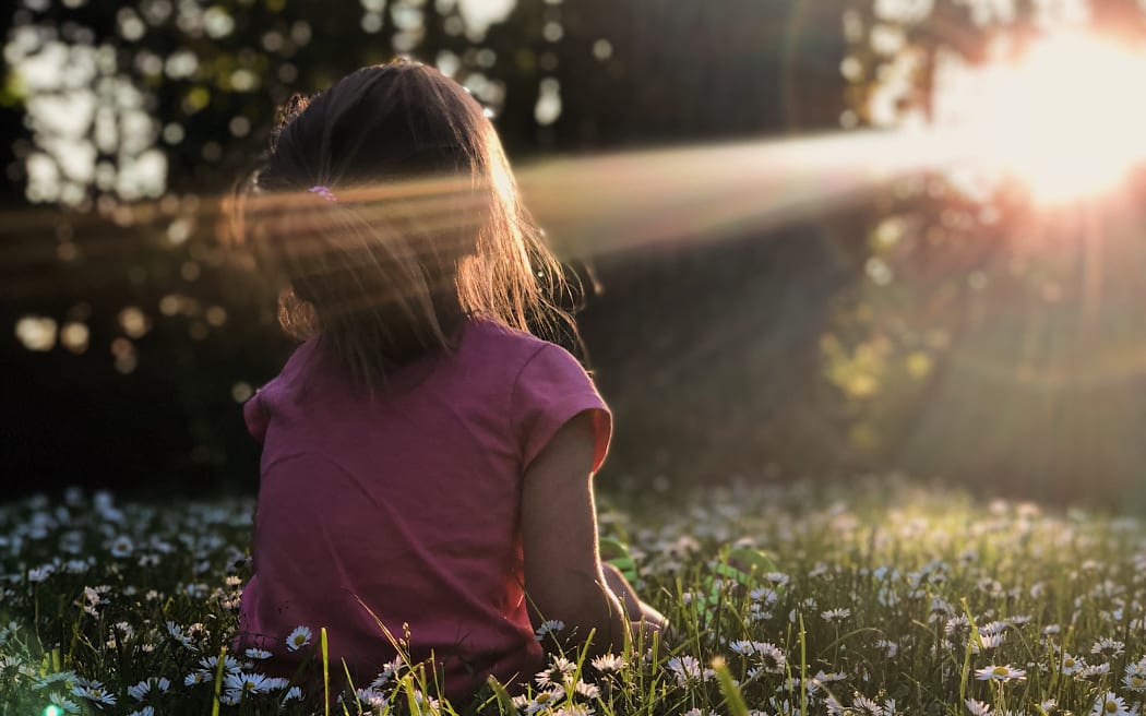 a child in a field of flowers facing the sun
