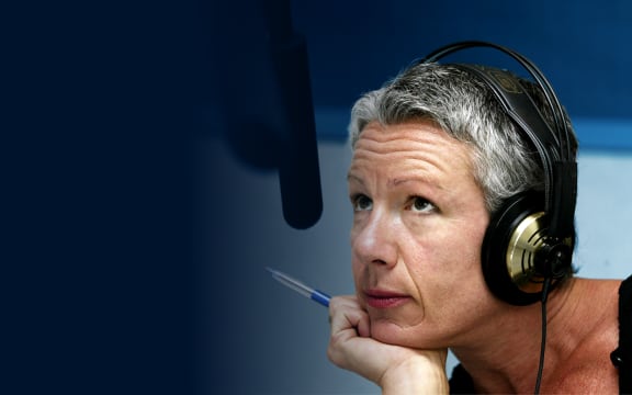 A thoughtful woman with short grey hair wearing headphones listens intently.
