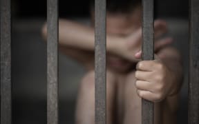 The child sat crying in a dark room separated by a steel cage. The concept of stopping violence against children and human trafficking.