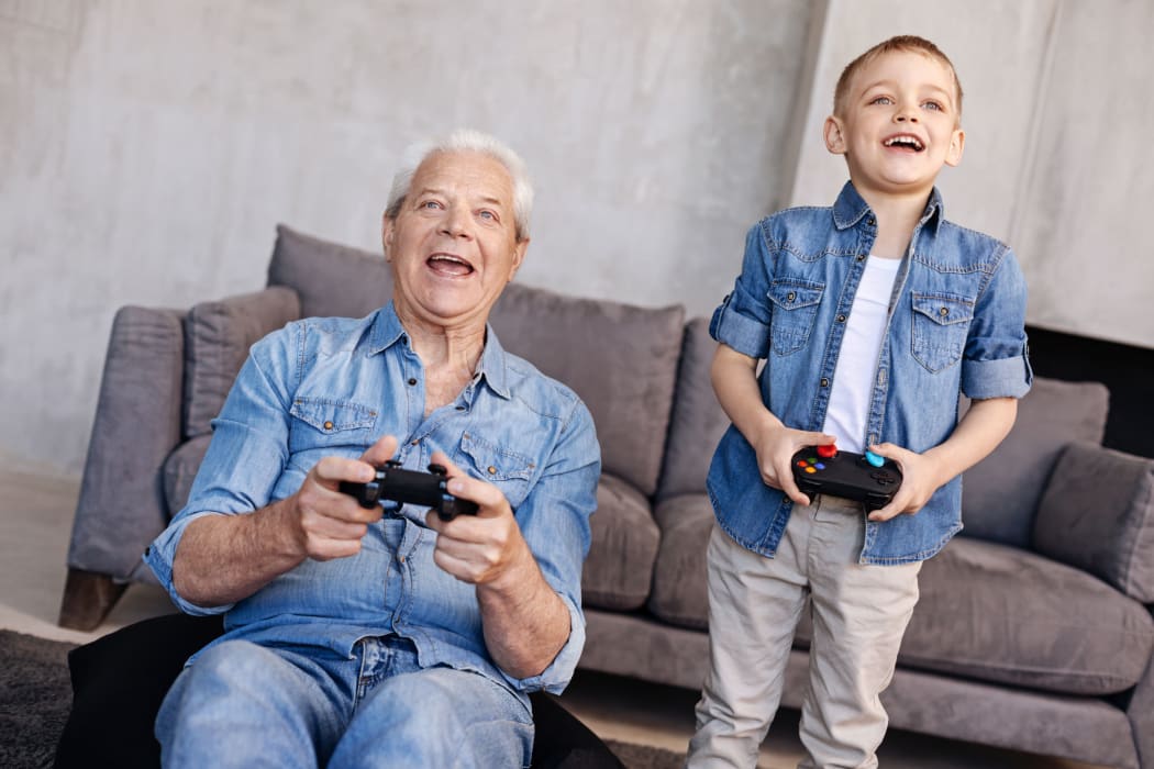 A photo of a boy teaching his father or grandfather how to game using a gaming controllers.