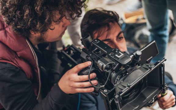 Behind the scene. Cameraman and assistant shooting the film scene with camera on outdoor location