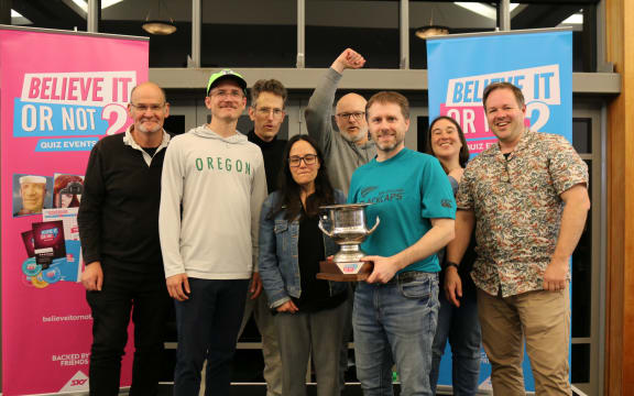 The champion quiz team “Eddie’s Back, Don’t Panic!” with team captain Kelvin Lange holding the trophy.