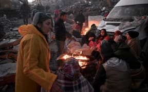 People stand near a bonfire amidst the rubble of collapsed buildings in Kahramanmaras, on February 8, 2023, two days after a 7,8-magnitude earthquake struck southeast Turkey. - Searchers were still pulling survivors on February 8 from the rubble of the earthquake that killed over 11,200 people in Turkey and Syria, even as the window for rescues narrowed. For two days and nights since the 7.8 magnitude quake, thousands of searchers have worked in freezing temperatures to find those still alive under flattened buildings on either side of the border. (Photo by OZAN KOSE / AFP)