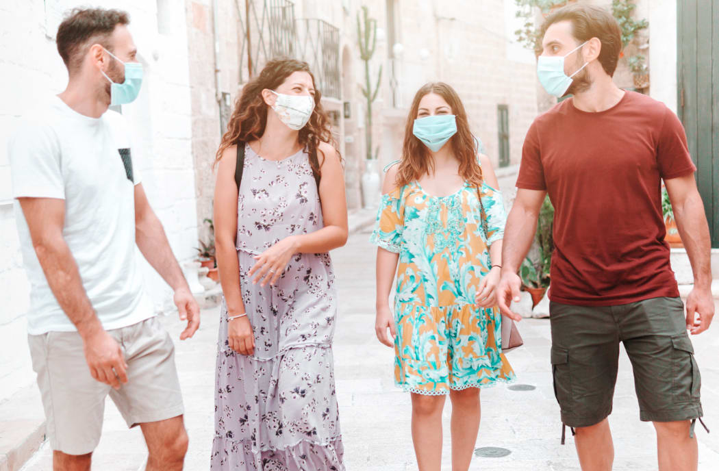 Group of friends stroll through city streets wearing surgical masks - people walk wearing protective equipment during the coronavirus pandemic